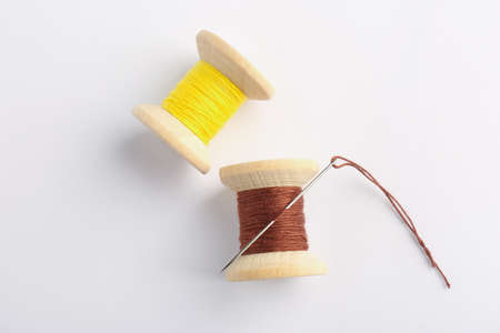 Colorful sewing threads with needle on white background, top view