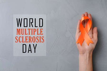 Multiple Sclerosis Awareness Day. Woman holding orange ribbon on light gray background, top view
