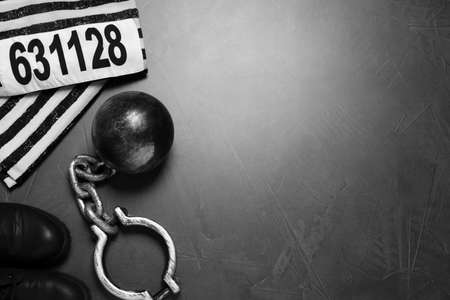 Prisoner ball with chain and jail clothes on gray table, flat lay. Space for text