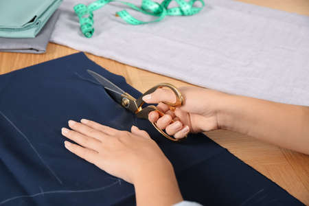 Woman cutting blue fabric with scissors at wooden table, closeup