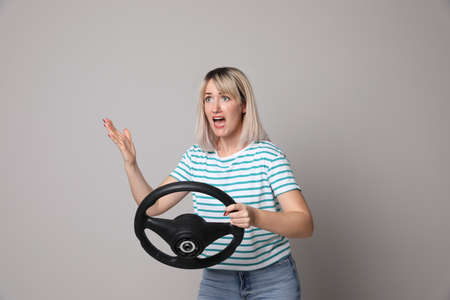Emotional woman with steering wheel on grey background