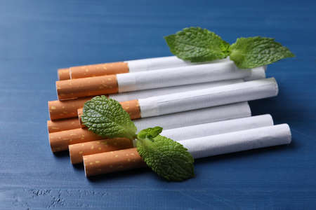 Menthol cigarettes and mint leaves on blue wooden tableの写真素材