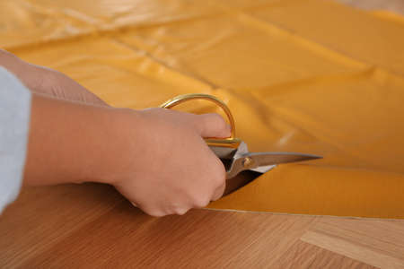 Woman cutting orange leather with scissors at wooden table, closeupの写真素材