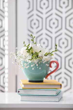 Beautiful bright flowers in cup and books on white table indoorsの写真素材