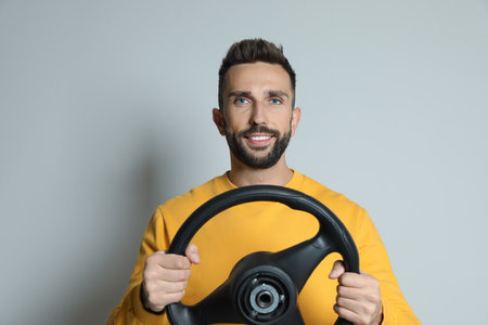Happy man with steering wheel on gray background