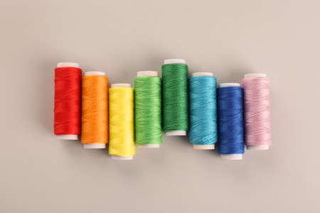 Different colorful sewing threads on light grey background, flat lay