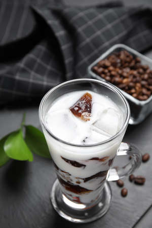 Glass cup of milk with delicious grass jelly and coffee beans on black table, closeup