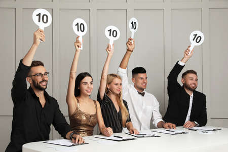 Panel of judges holding signs with highest score at table against light wallの写真素材