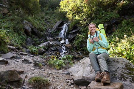 Tourist with cup near waterfall in mountains. Space for text