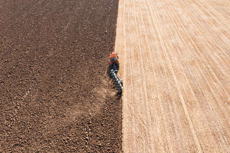 Tractor pulling plow in agricultural field on sunny day, aerial viewの写真素材