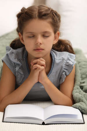 Cute little girl praying over Bible in bedroomの写真素材