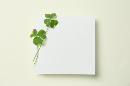 Green clover leaves and blank card on light background, top view. Space for text