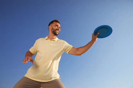 Happy man catching flying disk against blue sky on sunny day, low angle viewの写真素材