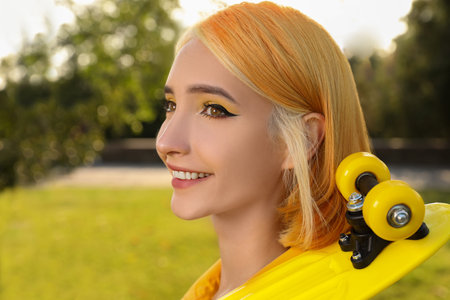 Beautiful young woman with bright dyed hair holding penny board in parkの写真素材