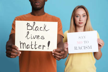 Young woman and African American man holding signs on light blue background, closeup. Racism concept