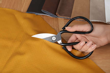 Woman cutting orange leather with scissors at wooden table, closeupの写真素材