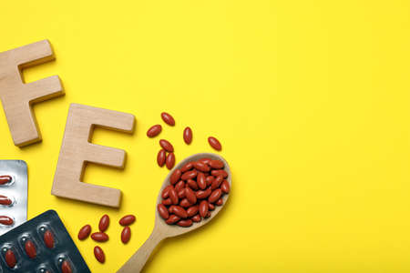 Wooden letters FE and pills on yellow background, flat lay with space for text. Anemia treatment