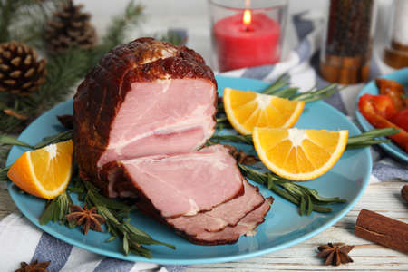 Plate with delicious ham, rosemary and orange on white wooden table. Christmas dinner