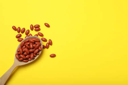 Wooden spoon with pills on yellow background, flat lay. Space for textの写真素材