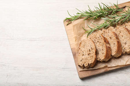 Cut buckwheat baguette with rosemary on white wooden table, top view. Space for text