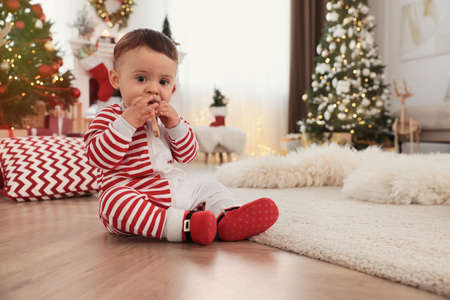 Cute baby wearing bright pajamas on floor in room decorated for Christmas