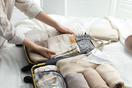 Woman packing suitcase for trip on bed, closeup