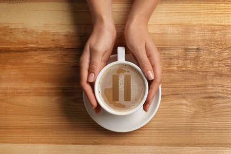 Coffee Break. Woman holding cup of americano with milk at wooden table, top viewの写真素材