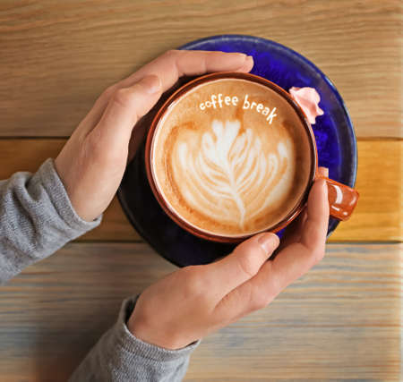 Coffee Break. Woman with cup of cappuccino at wooden table, top view