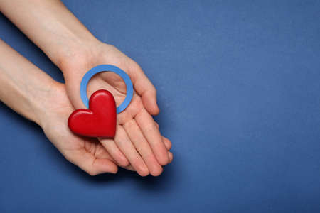 Woman showing blue paper circle as World Diabetes Day symbol and red heart on color background, top view with space for textの写真素材