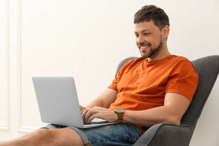 Happy man using laptop in armchair indoors. Internet shoppingの写真素材