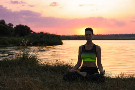 Mature woman meditating near river at sunset. Space for textの写真素材