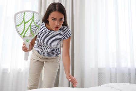 Young woman with electric fly swatter in bedroom. Insect killerの写真素材