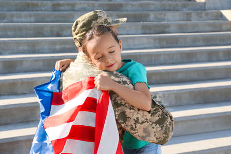 Soldier with flag of USA and his little daughter hugging outdoors, space for textの写真素材