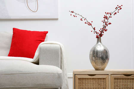 Hawthorn branches with red berries on wooden commode in living roomの写真素材