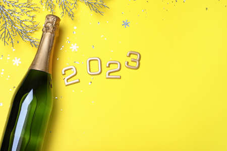 Happy New Year 2023! Flat lay composition with bottle of sparkling wine on yellow background, space...