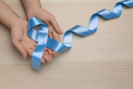 Woman holding light blue awareness ribbon at wooden table, top view. Space for textの写真素材