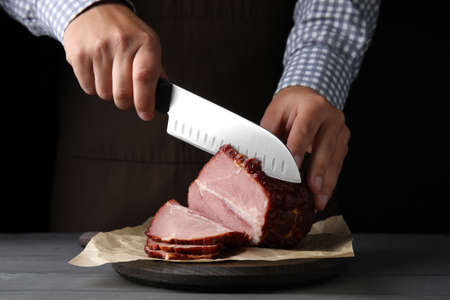 Man cutting ham on wooden board at table, closeup