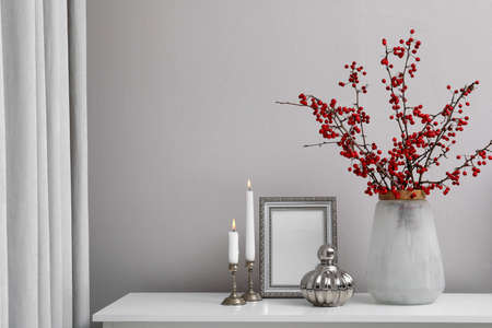 Hawthorn branches with red berries in vase, candles and frame on table indoors, space for textの写真素材