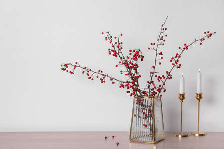 Hawthorn branches with red berries in vase and candles on wooden table, space for textの写真素材