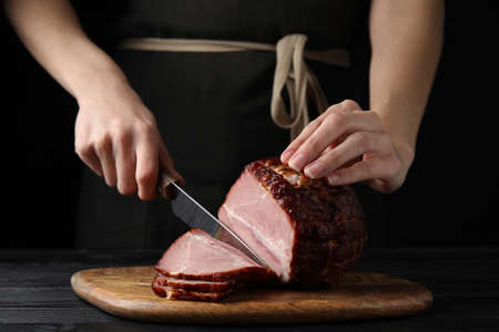 Woman cutting ham on wooden board at table, closeupの写真素材