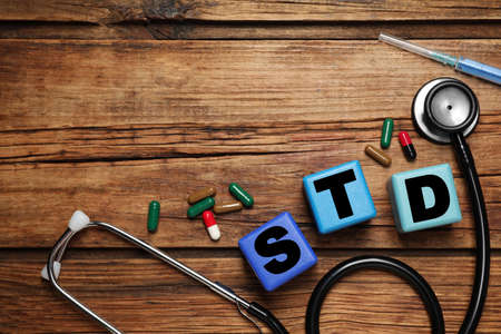 Colorful cubes with letters STD, capsules, stethoscope and syringe on wooden table, flat lay. Space for textの写真素材