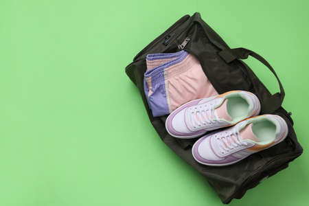 Sports bag with sneakers and clothes on light green background, top view. Space for text