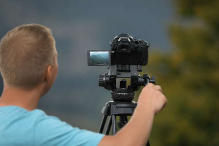 Photographer taking video with modern camera on tripod in nature