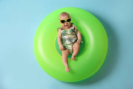 Cute little baby in sunglasses with inflatable ring on light blue background, top viewの写真素材