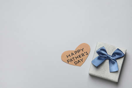 Heart shaped card with phrase HAPPY FATHER'S DAY and gift box on light gray background, flat lay....