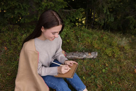 Young woman drawing with pencil in sketchbook near forest, space for textの写真素材
