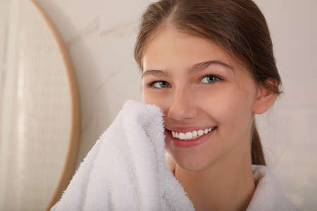 Beautiful teenage girl wiping face with towel at home, closeupの写真素材