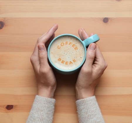 Coffee Break. Woman with cup of cappuccino at wooden table, top viewの写真素材