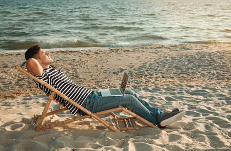 Man with laptop relaxing in deck chair on beachの写真素材