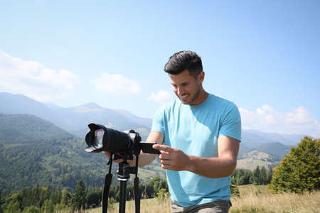 Professional photographer taking picture with modern camera in mountains